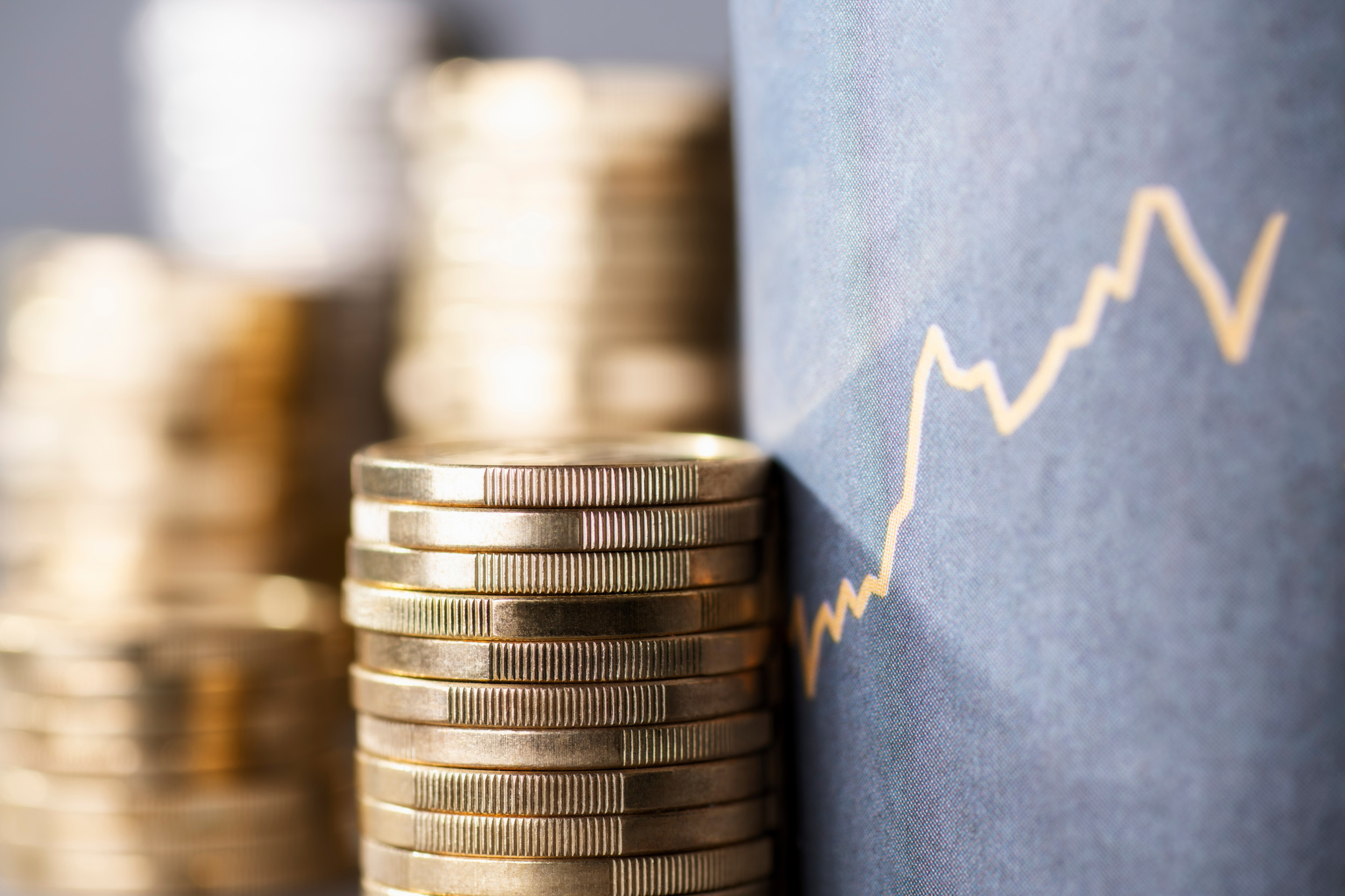 gestappelte Euromünzen neben einen steigen Kurschart mit blauen Hintergrund.
