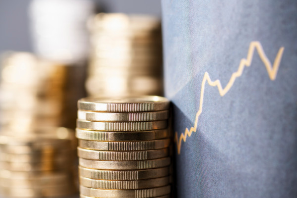 gestappelte Euromünzen neben einen steigen Kurschart mit blauen Hintergrund.