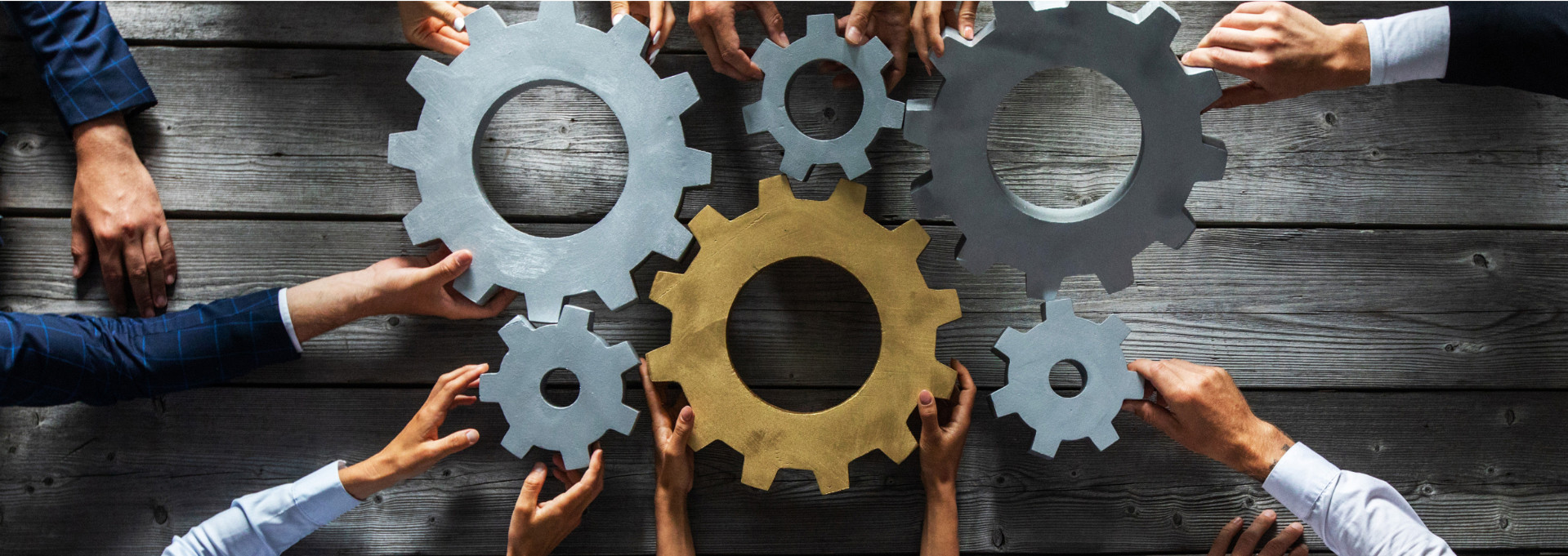 Es liegen große Zahnräder auf einem Holztisch. Der Blick von oben. Hände drehen die Zahnräder.