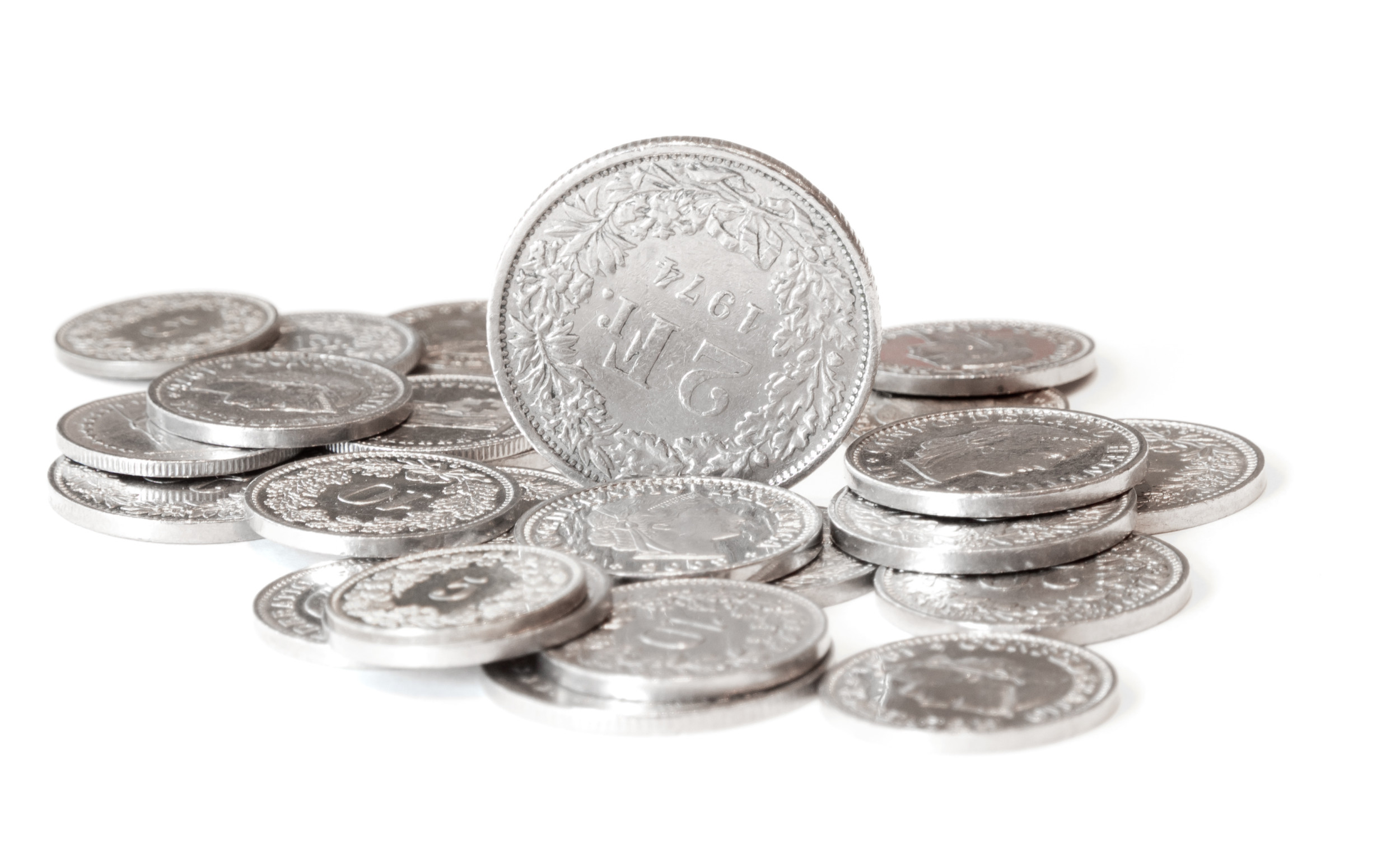 mehre Münzen von Schweizer Franken die liegen und eine die aufrecht steht und man die Zahl 2 erkennt.