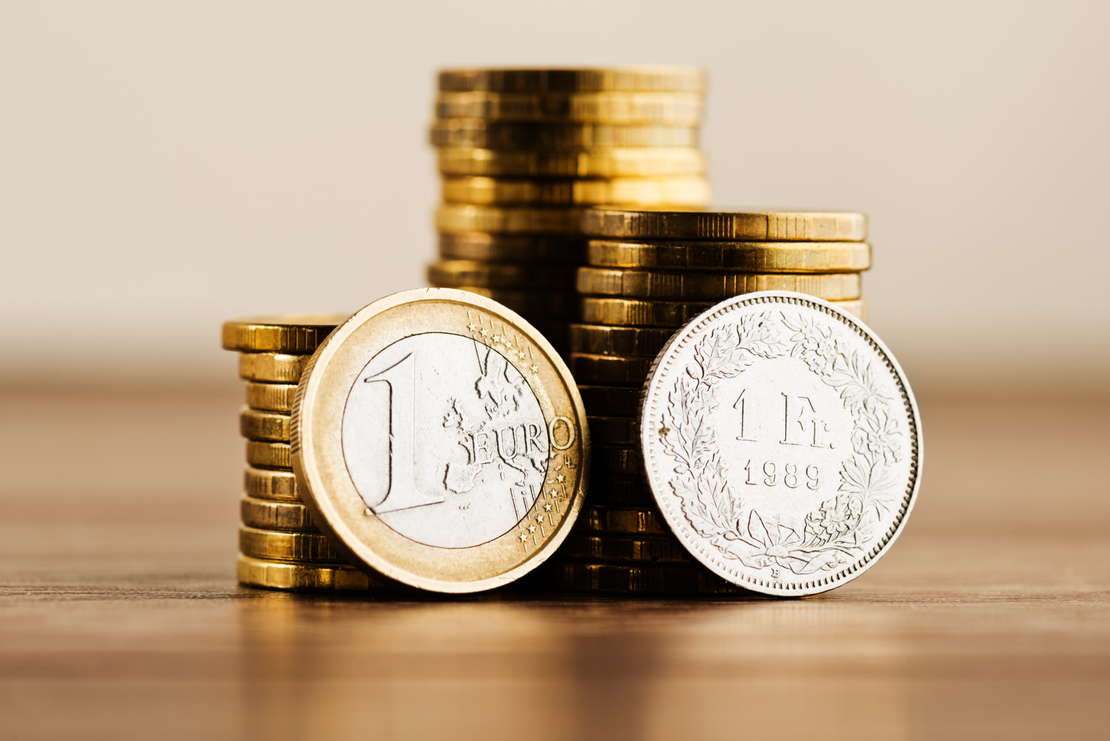 Münzen die gestappelt auf einem Holztisch liegen und man erkennt eine Euro-Münze und eine Schweizer Franken Münze.