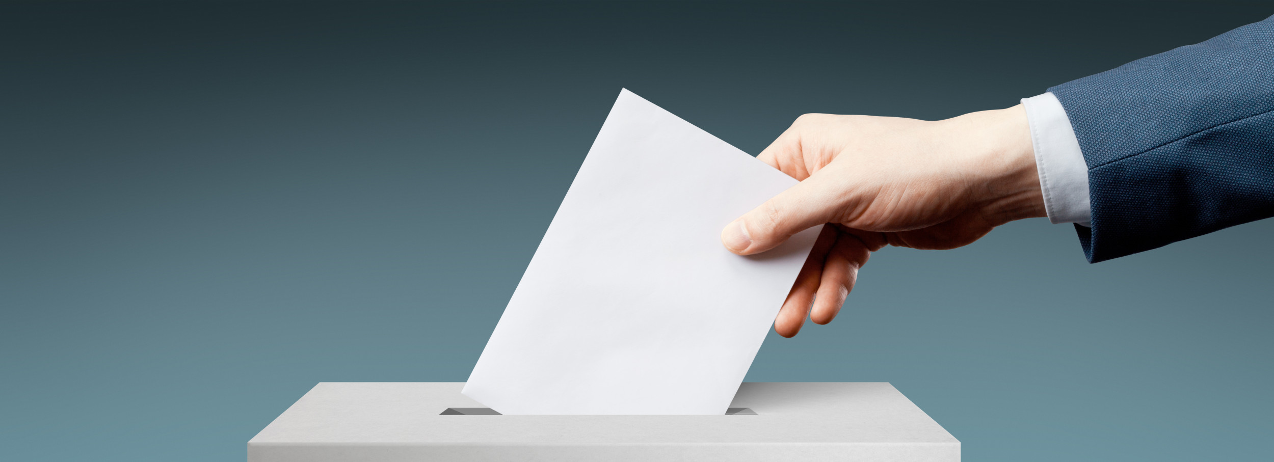 Eie Wahlurne in den ein Umschlag von einer Wahl hineingesteckt wird.