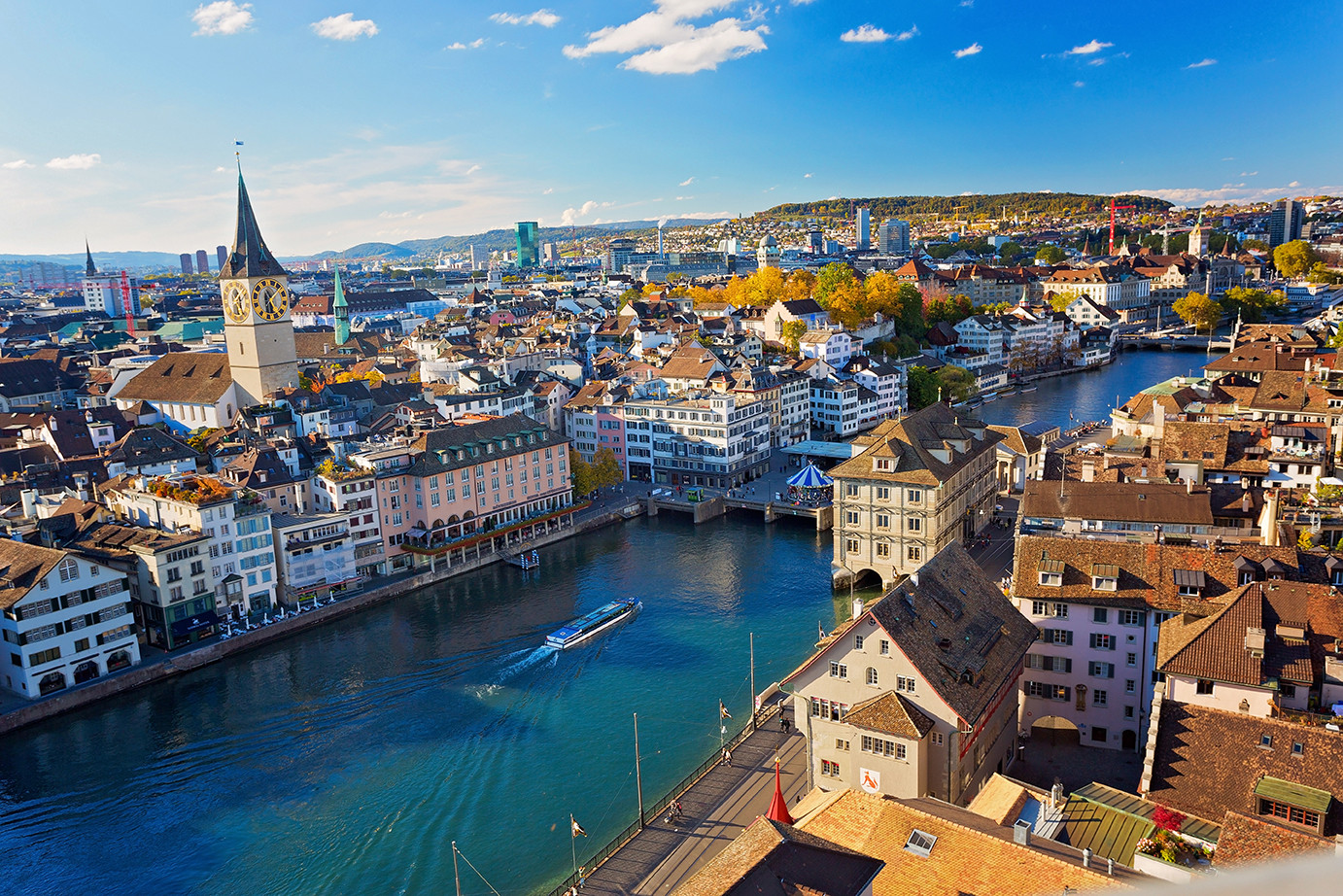 Die Stadt Zürich aus der Luft bei blauen Himmel. Auf der ruhigen Limmat fährt ein Schiff.